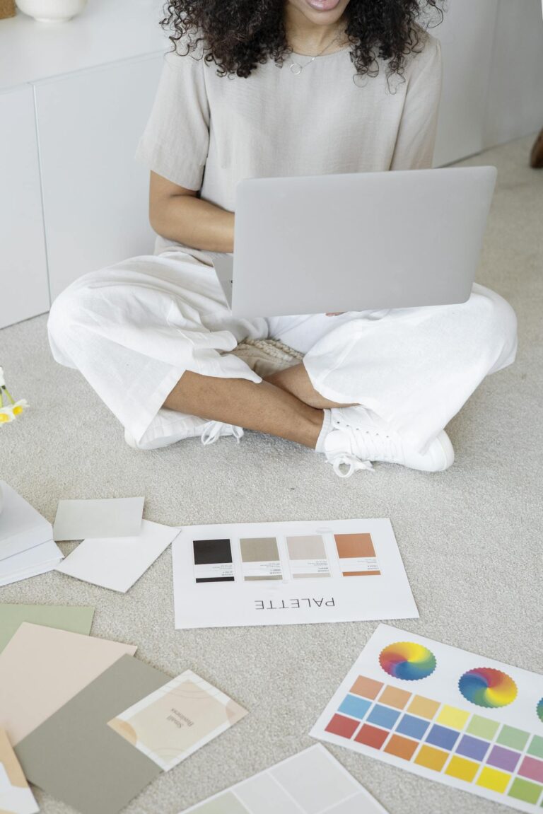 Young woman reviews color palettes for design project on laptop, sitting indoors.